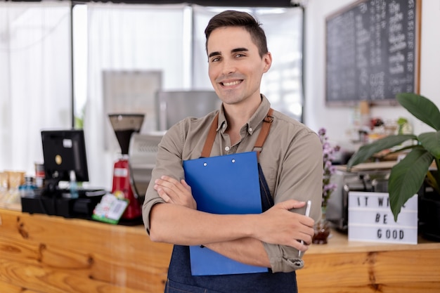 Ein gutaussehender Mann, der in einem Café steht, er ist ein Café-Arbeiter, er bereitet sich darauf vor, einen Laden zu eröffnen, um Kunden zu bedienen, ein männlicher Angestellter eröffnet einen Laden, um Speisen und Getränke zu servieren. Servicekonzept für Speisen und Getränke.