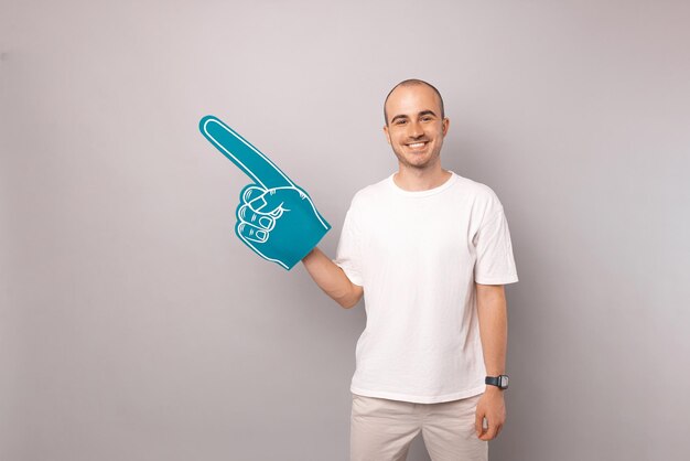 Ein gutaussehender Mann mit Glatzenbildung trägt einen Schaumstoff-Fan-Fingerhandschuh auf grauem Hintergrund