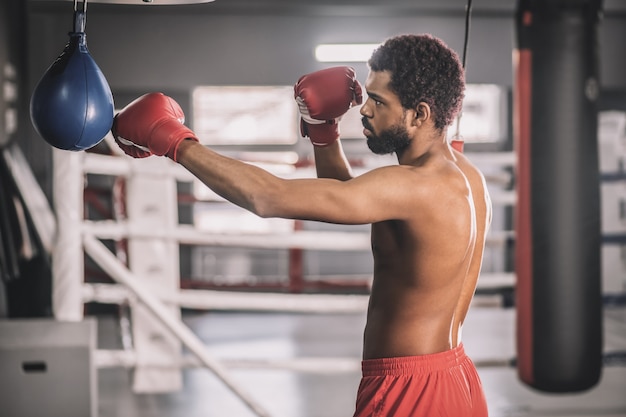 Ein guter Kick. Afroamerikanischer Kickboxer, der in einem Fitnessstudio trainiert und den Sandsack tritt