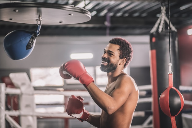 Ein guter Kick. Afroamerikanischer Kickboxer, der in einem Fitnessstudio trainiert und den Sandsack tritt