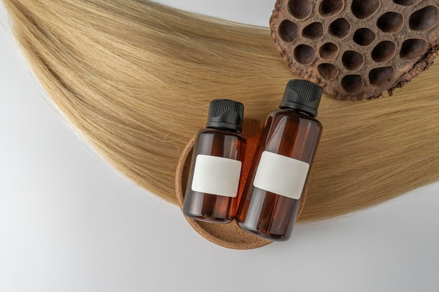 Ein Haarpflegeöl oder -serum in braunen Tropfflaschen, die auf einem Marketingmodell für blonde Haarsträhne liegen