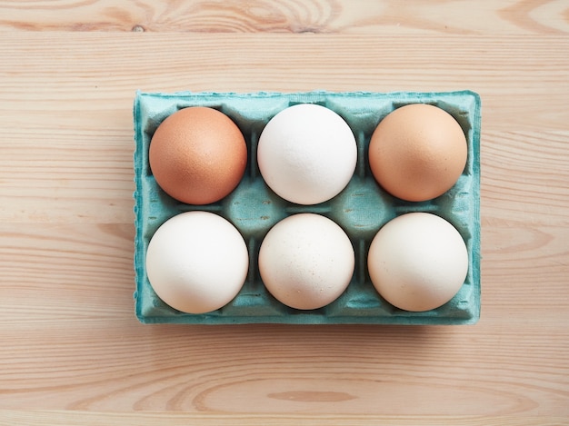 Ein halbes Dutzend frische rohe Eier braun und weiß in einem grünen Karton auf einem Holztisch