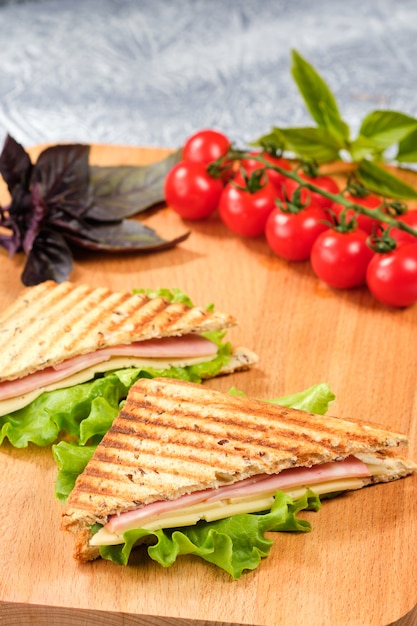 Ein halbes Sandwich in Form eines Dreiecks auf einem Holzbrett. Das Sandwich ist mit einem Salatblatt und Kirschtomaten dekoriert.