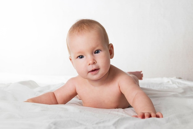 Ein halbjähriges schönes Baby in einer Windel liegt auf dem Bauch und schaut mit unterschiedlichen Emotionen auf die Kamera