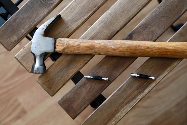 ein hammer auf einem holzstuhl, dahinter ein brettteil eines grauen schreibtisches.