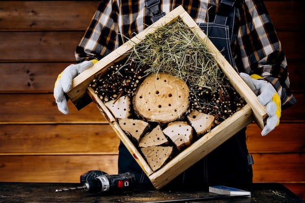 Ein Handwerker, der ein Holzhaus für Insekten herstellt Ein Zimmermann, der in der Werkstatt ein Werkzeug verwendet