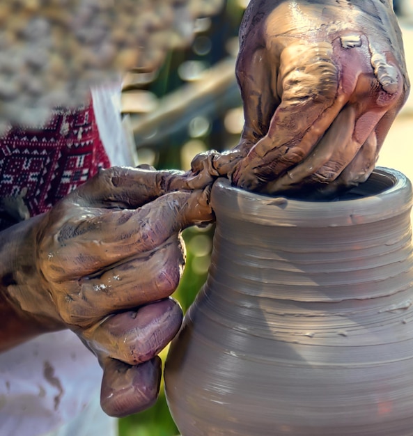 Ein Handwerker stellt ein Keramikprodukt auf einer Töpferscheibe her. Die Hände sind mit rohem Ton bedeckt