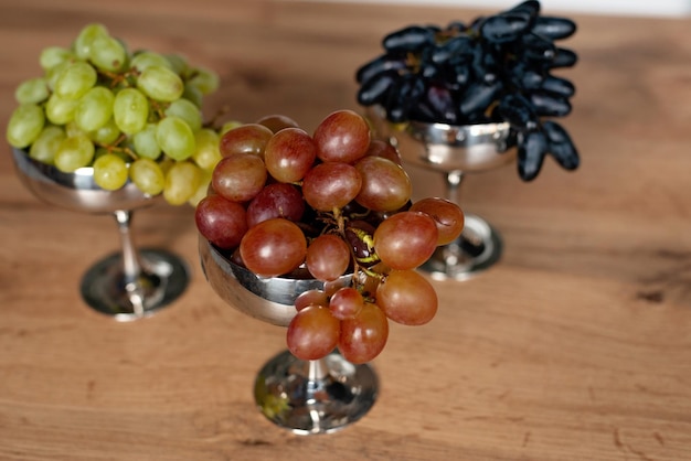Ein Haufen blauer, grüner und roter Trauben in Metallschalen auf einem Holztisch. Gesunde Ernährung. Weicher selektiver Fokus