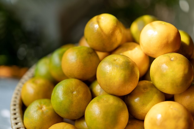 Ein Haufen Orangen auf einer Bambusweidenplatte in goldenem Licht auf unscharfem grünem Naturhintergrund