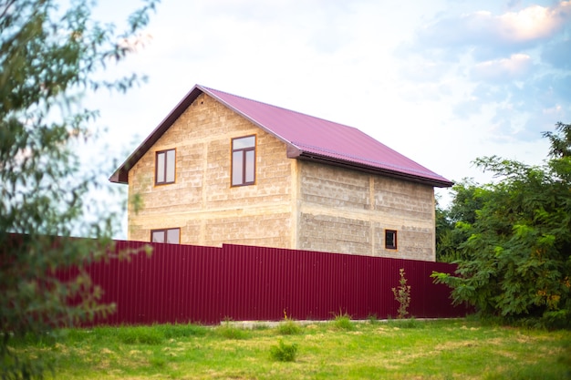Ein Haus mit einem purpurroten Dach hinter einem Zaun in einem Dorf im Sommer. Bau von Vorstadtwohnungen.
