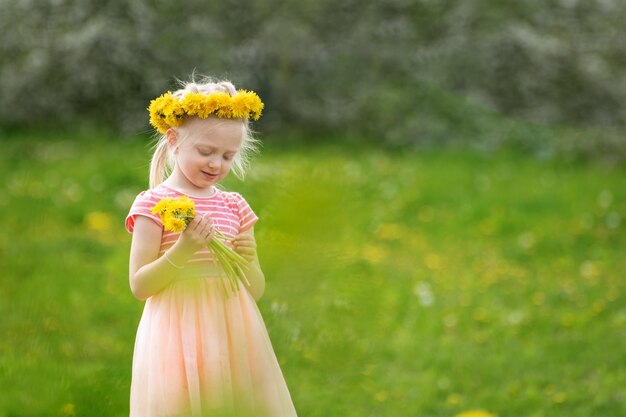 Ein hellhaariges Kind auf einem Feld mit gelben Löwentieren, eine kleine Dame in einem rosa Kleid, die Blumen hält, ein selektiver Fokus.