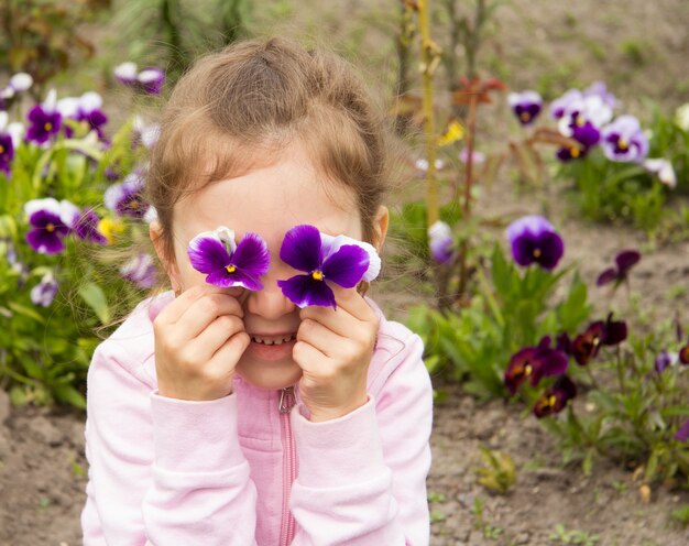 Foto ein hellhäutiges fünfjähriges mädchen legte blumen auf ihre augendas sind blaue und violette stiefmütterchen