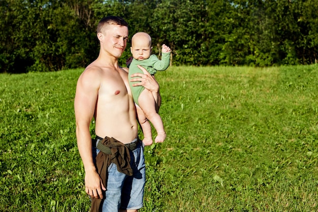 Ein hemdloser Europäer hält ein Baby auf dem Land in den Armen