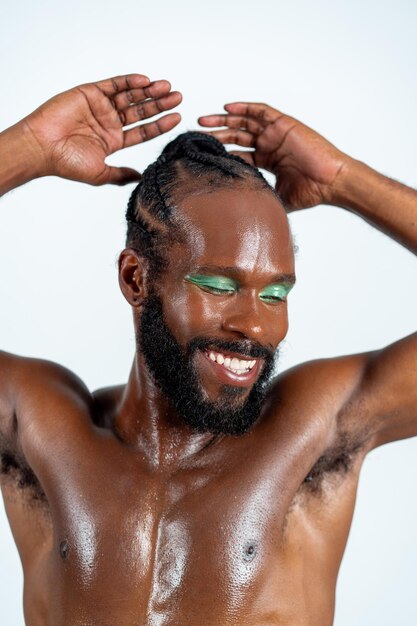 Ein hemdloser schwuler Mann mit hellem Make-up lächelt in einem weißen Studio.