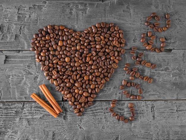 Ein Herz aus Kaffeebohnen und zwei Zimtstangen auf einem schwarzen Holztisch. Der Blick von oben. Getreide zur Zubereitung des beliebten Getränks.