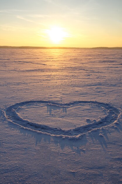 Ein Herz wird in den Schnee gezeichnet. Sonnenuntergang im Hintergrund.