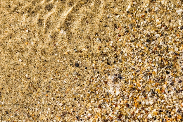 Ein Hintergrund aus kleinen Kieselsteinen und fließenden Wellen am Meeresstrand Sommerurlaubskonzept