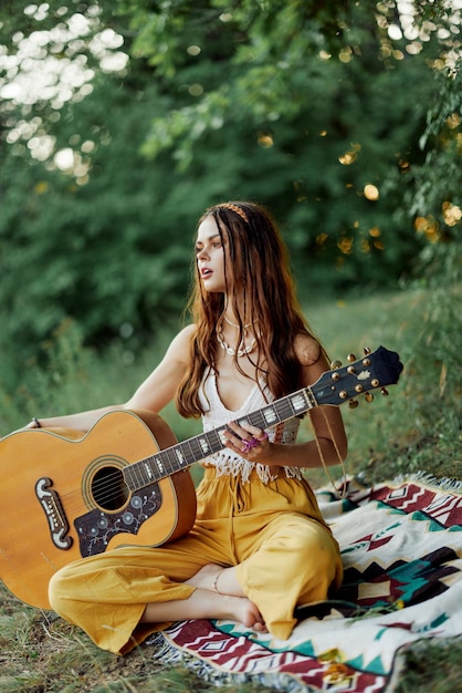 Ein Hippie-Mädchen in Öko-Kleidung sitzt mit einer Gitarre und blickt auf einen Sonnenuntergang im Sommer