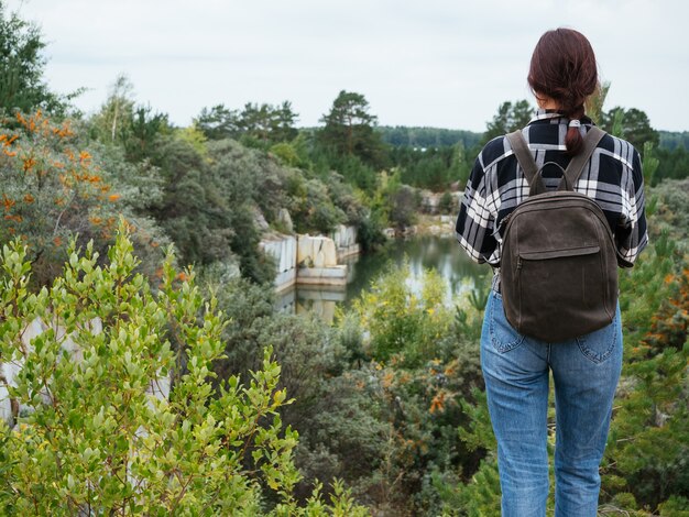 Ein Hipster-Mädchen in bequemer Freizeitkleidung steht an einer Klippe mit Blick auf den See