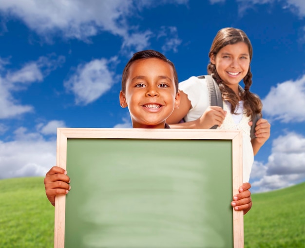 Ein Hispanic-Junge und ein Hispanic-Mädchen auf dem Feld mit einer leeren Kreidetafel