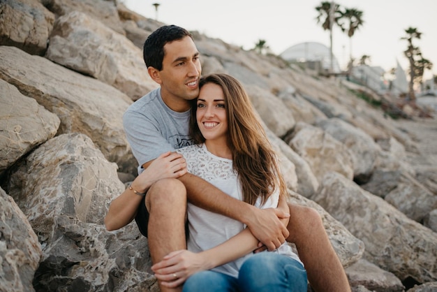 Ein Hispanoamerikaner sitzt mit seiner Freundin auf den Steinen eines Wellenbrechers