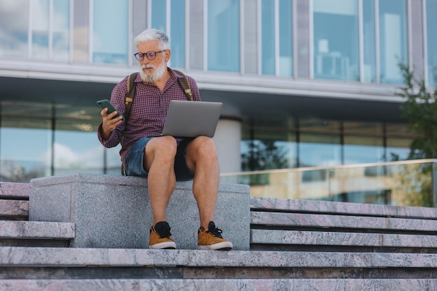 Ein hochrangiger Geschäftsmann, ein erwachsener Mann mit grauem Haar, arbeitet an einem Outdoor-Laptop im Büro eines Unternehmens