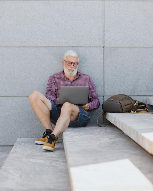 Ein hochrangiger Geschäftsmann, ein erwachsener Mann mit grauem Haar, arbeitet an einem Outdoor-Laptop im Büro eines Unternehmens