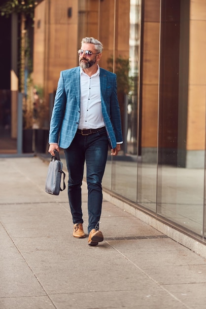 Ein hochrangiger Geschäftsmann in einem blauen Anzug mit einer Aktentasche, der durch die Stadt geht.