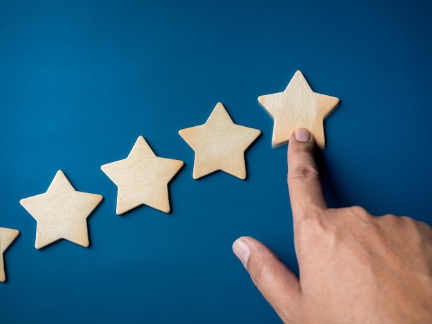 Ein hölzerner Stern, der von Hand von fünf Sternen als Diagrammschritt auf blauem Hintergrund nach oben geschoben wird Zufriedenheit Kundenbewertung Bewertung Qualität Belohnung Marketing Geschäftswachstum und Erfolgskonzepte