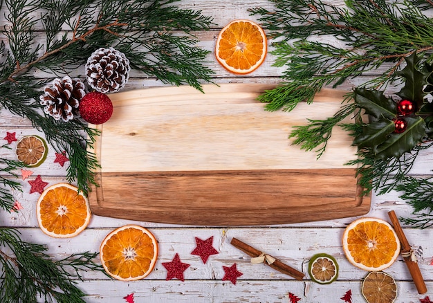 Ein hölzernes Brett mit Kopienraum für Text im Weihnachtsdekor mit Weihnachtsbaum, trockener Orange und Kegel auf Hintergrund