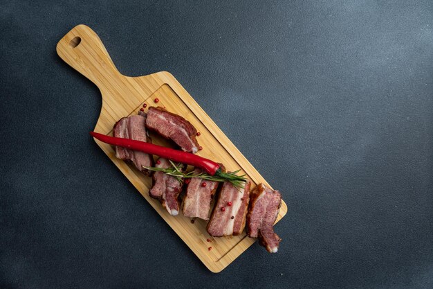 Ein hölzernes Schneidebrett mit Fleischscheiben und einer roten Paprika darauf.