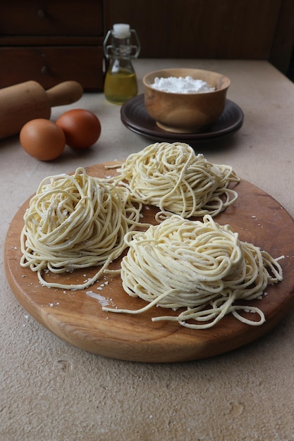 Ein hölzernes Schneidebrett mit Spaghetti darauf und eine Schüssel Eier im Hintergrund.