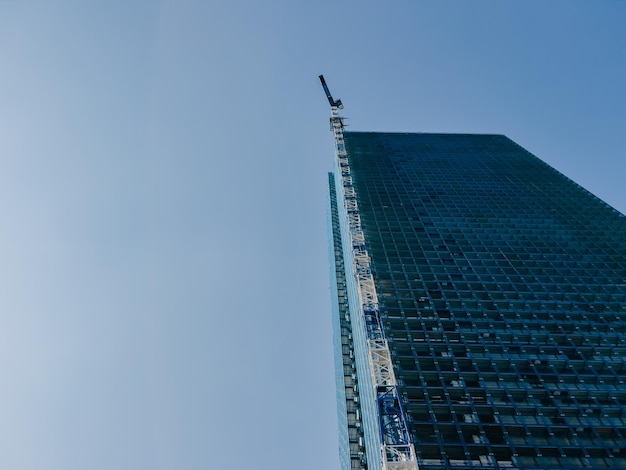 Ein hoher Turmkran baut einen riesigen Wolkenkratzer vor einem blauen Himmel