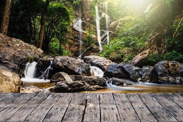 Ein Holzbrett in einem Wald mit einem Wasserfall im Hintergrund.