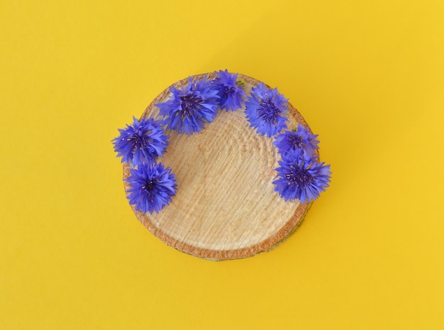 Ein Holzpodium mit blauen Kornblumen auf gelbem Grund zur Präsentation von Naturprodukten