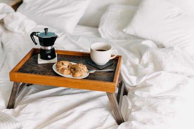 ein Holztablett mit Croissants und einer Tasse Kaffee auf dem Bett