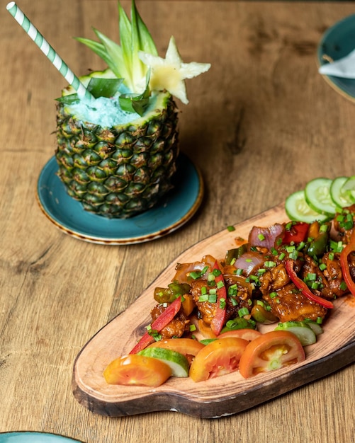 Ein Holztablett mit einer Ananas und ein Teller mit Essen mit einem Strohhalm, auf dem „Gurke“ steht