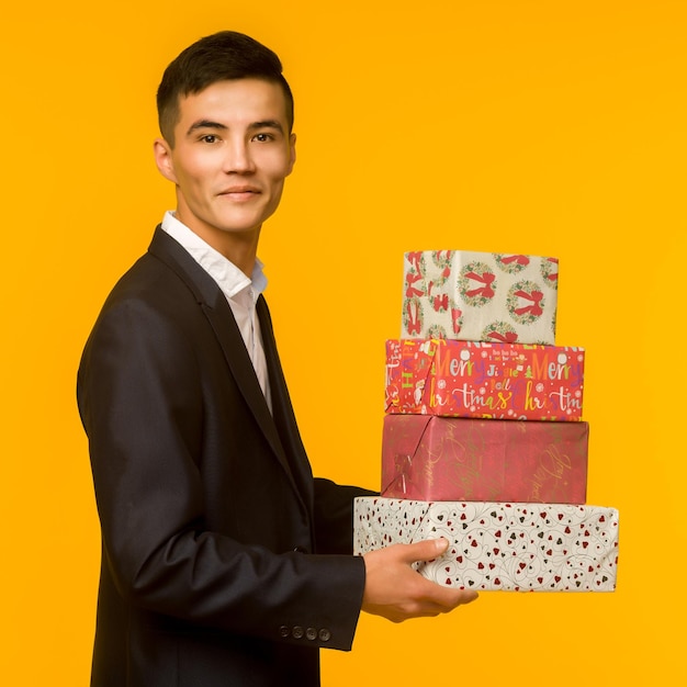 Ein hübscher asiatischer Geschäftsmann hält eine Geschenkkiste über einem gelben Hintergrundbild