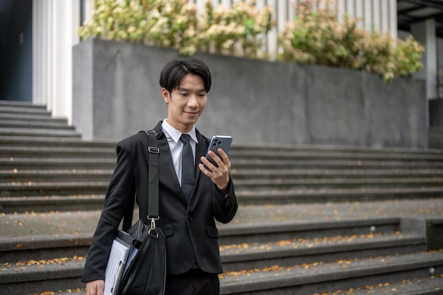 Ein hübscher asiatischer Geschäftsmann überprüft Nachrichten auf seinem Handy, während er die Treppe hinuntergeht