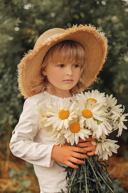 Foto ein hübscher blonder junge mit strohhut und leinenanzug mit gänseblümchen in den händen