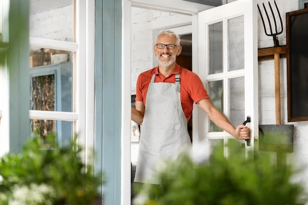 Ein hübscher, erwachsener Mann mit Schürze öffnet die Tür und begrüßt das Innere des Landhauses