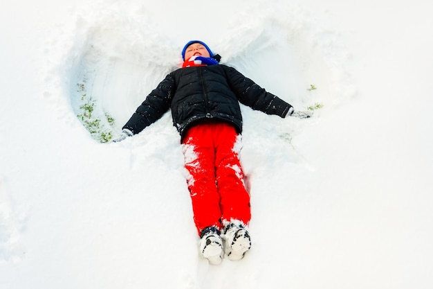 Ein hübscher Junge im Winter zeigt einen Engel an seinem Fuß