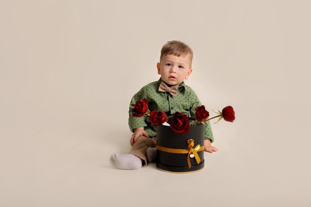 Ein hübscher Junge in einem grünen Hemd sitzt neben einer Kiste mit roten Rosen auf weißem Hintergrund