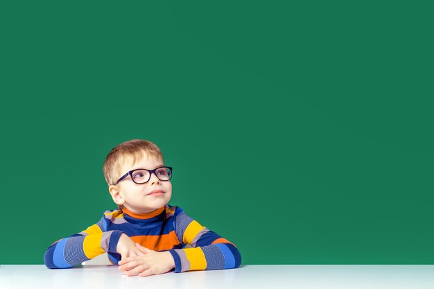 Ein hübscher Junge mit Brille sitzt am Tisch und schaut weg Kopieren Sie Platz