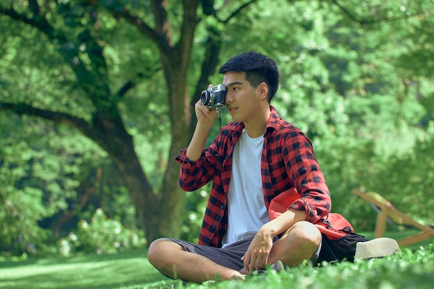 Ein hübscher junger asiatischer Mann sitzt im Sommer auf dem Rasen im Park.