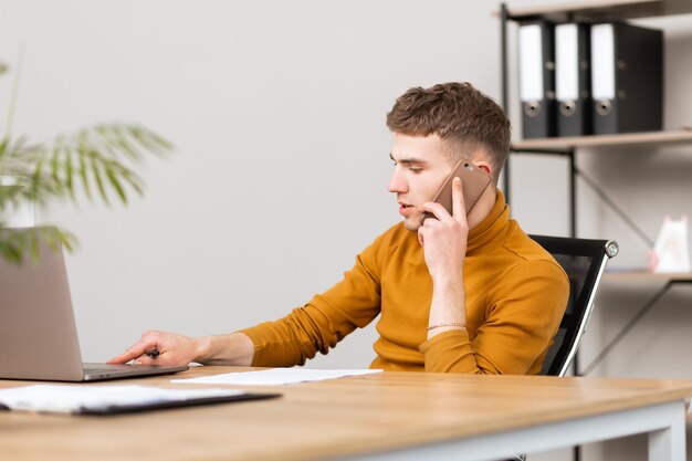 Ein hübscher junger Mann arbeitet mit Dokumenten im Büro und löst Probleme per Telefon