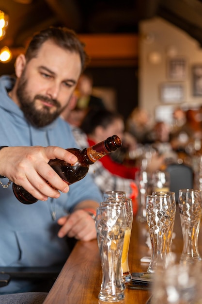 Ein hübscher junger Mann mit Bart, der Bier aus einer Flasche in Gläser gießt