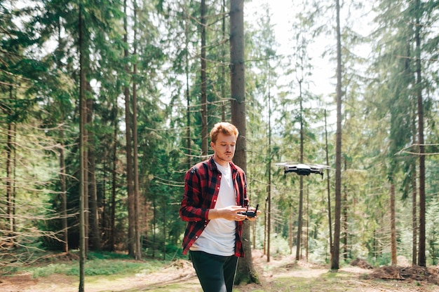 Ein hübscher junger Mann steuert eine Drohne im Wald und schaut aufmerksam auf die Fernbedienung