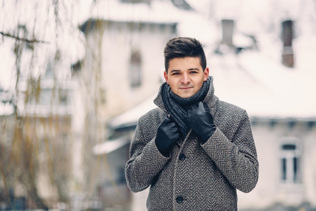 Ein hübscher lächelnder junger Mann in einem warmen Mantel und Lederhandschuhen beim Gehen auf der Stadt
