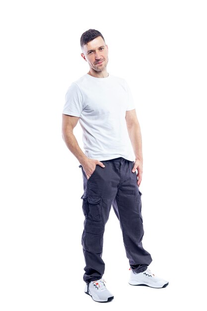 Ein hübscher, lächelnder Mann in weißem T-Shirt und dunkler Hose steht mit den Händen in den Taschen Positivität und Selbstvertrauen Vollhöhe Isoliert auf weißem Hintergrund Vertikaler Raum für Text